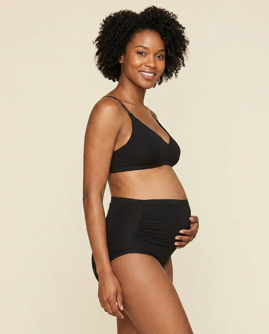 Woman wearing the triangle soft bra in carbon black and above-belly brief  in carbon black color against a solid light beige background.