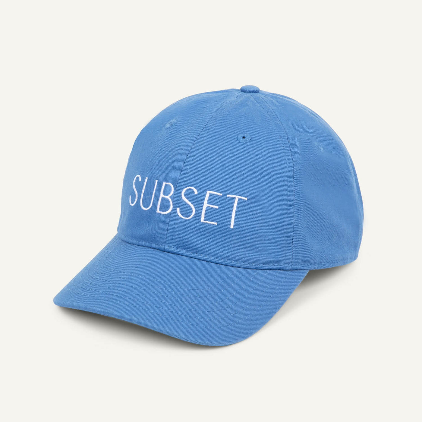 A blue organic cotton baseball cap with the word 'SUBSET' embroidered in white on the front.