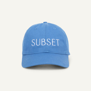 A blue organic cotton baseball cap with the word 'SUBSET' embroidered in white on the front.
